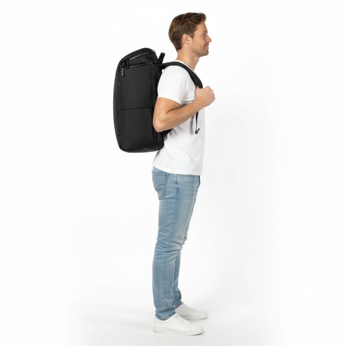 Mężczyzna w białej koszulce i dżinsach nosi czarny plecak Zeeksack, widok z boku.