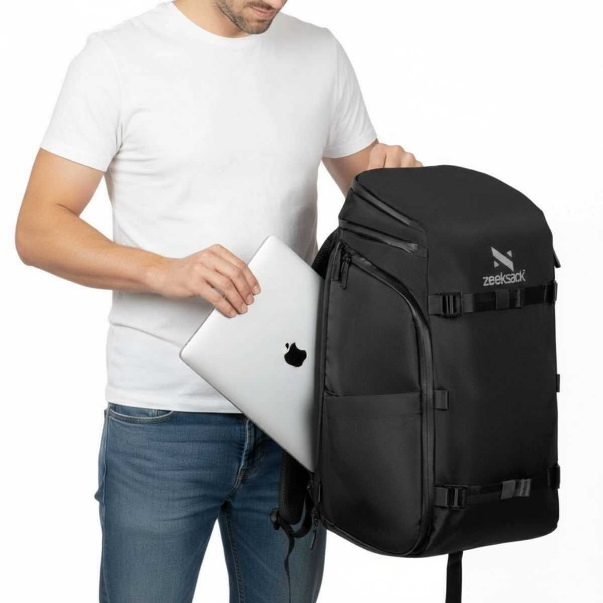 Mężczyzna w białej koszulce wkłada srebrny laptop do czarnego plecaka.