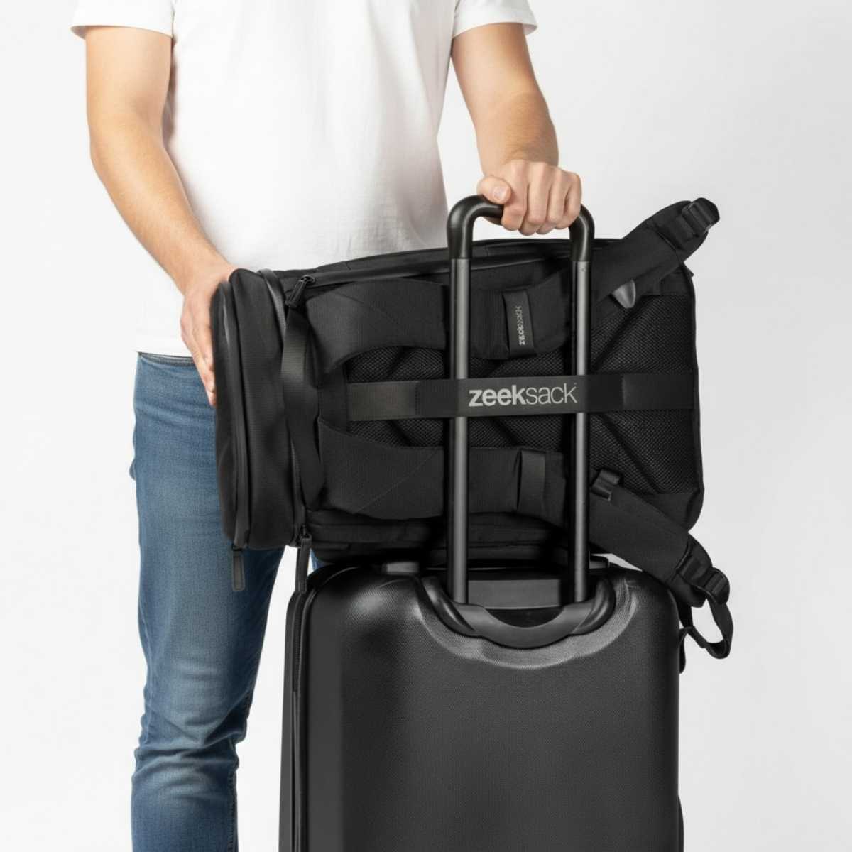 Czarny plecak Zeeksack umieszczony na rączce walizki podróżnej, studio na białym tle.