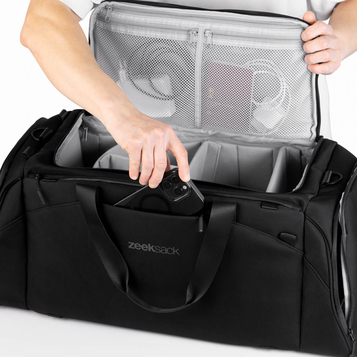 Torba Zeeksack The Duffelbag z przednią kieszenią – osoba wkłada smartfon do zewnętrznej przegrody.