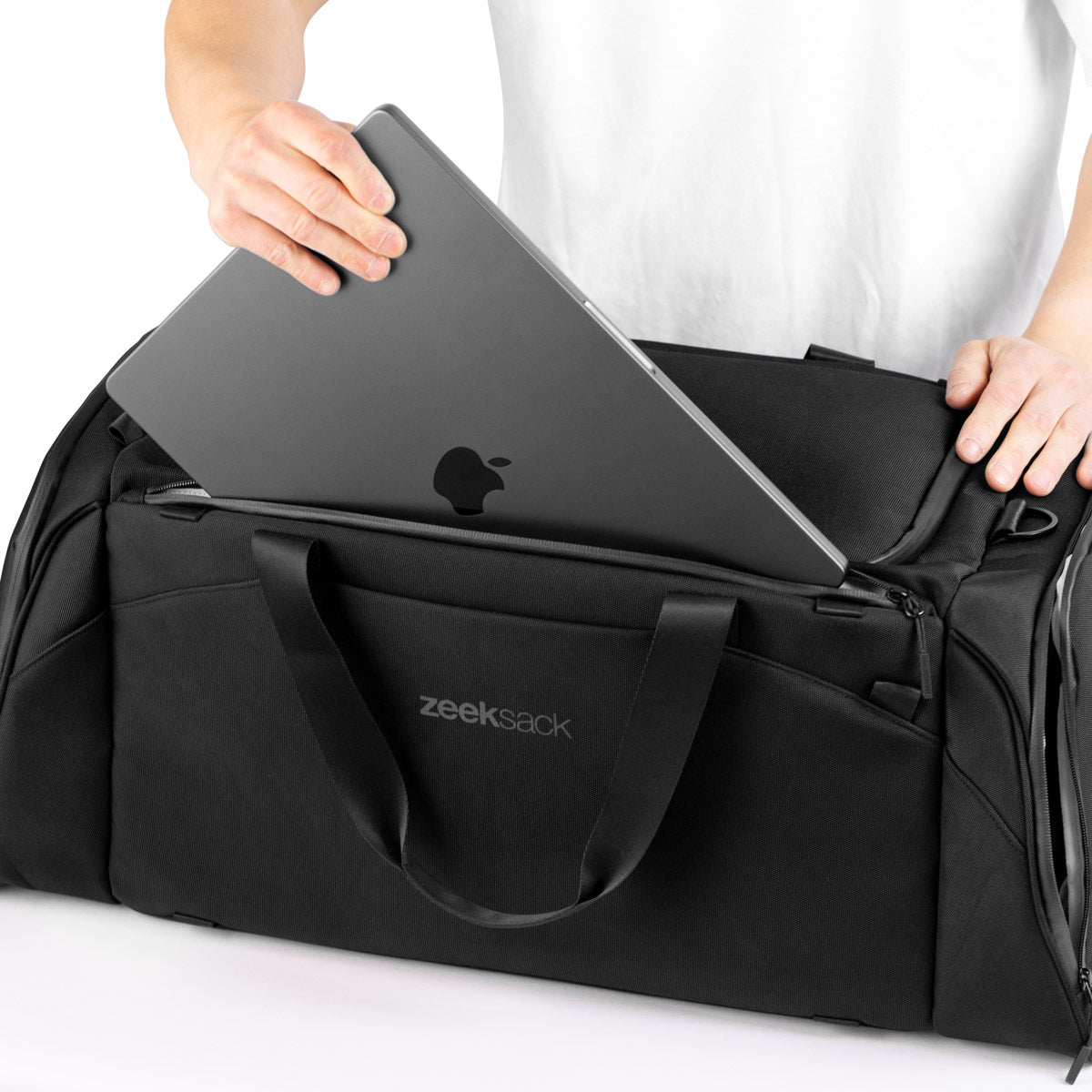 Torba Zeeksack The Duffelbag z osobną przegrodą na laptop – osoba wkłada komputer przenośny do górnej kieszeni.