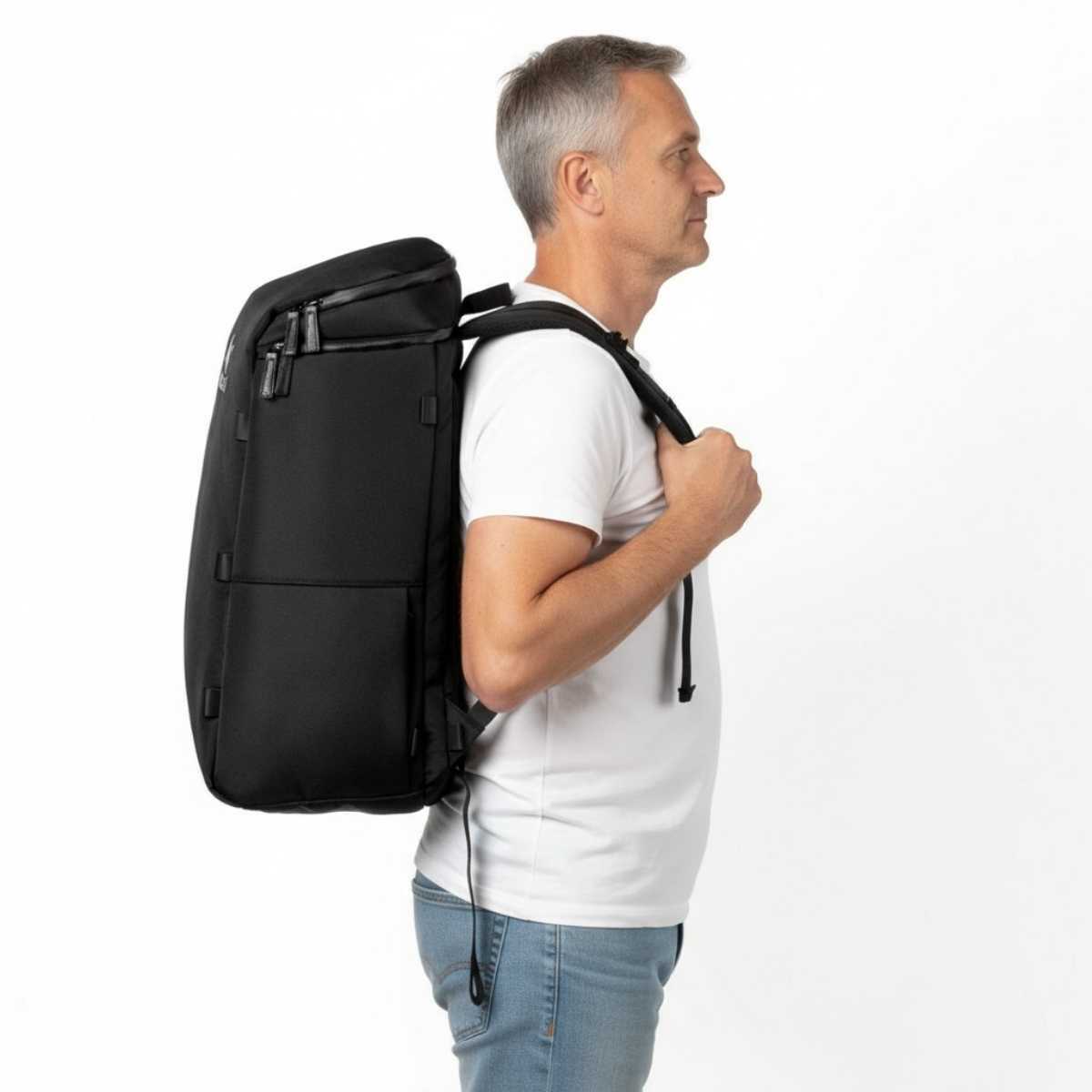 Mężczyzna w średnim wieku w białej koszulce i dżinsach pokazuje plecak Zeeksack w profilu, studio na białym tle.
