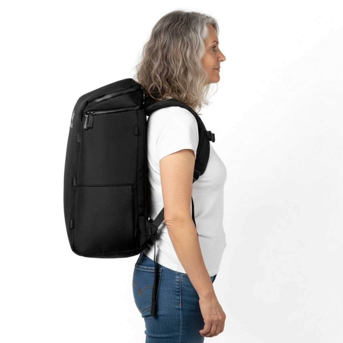Kobieta w średnim wieku w białej koszulce i dżinsach prezentuje plecak Zeeksack w profilu, studio na białym tle.