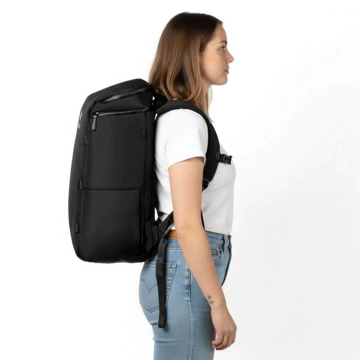 Kobieta w białej koszulce i dżinsach pokazuje plecak Zeeksack na plecach w profilu, studio na białym tle.
