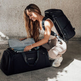 Kobieta w sportowym stroju korzysta z torby Zeeksack The Duffelbag – otwiera główną komorę, a na plecach ma drugi plecak Zeeksack.